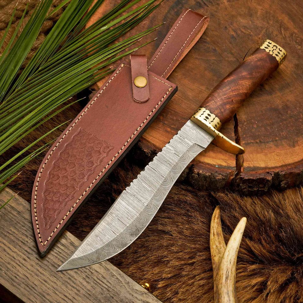 Hand-forged Damascus steel Bowie knife with burl wood handle and brass guard displayed next to a stamped brown leather sheath