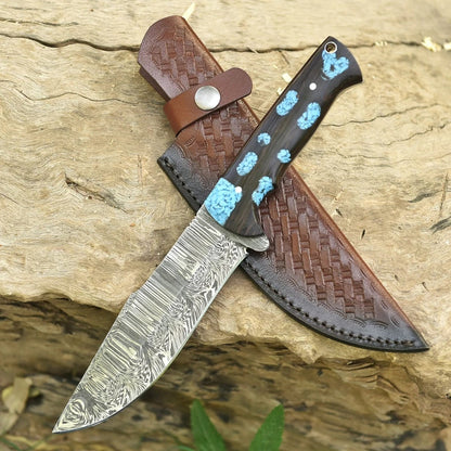 Hand-forged Damascus steel fixed blade knife with turquoise-inlaid dark wood handle crossed over a basketweave brown leather sheath on natural wood